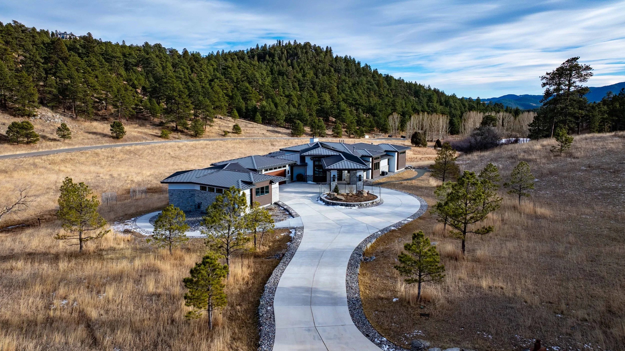 Aerial view of a Foothills Architects custom home with a curved drive, set in a pine-dotted meadow